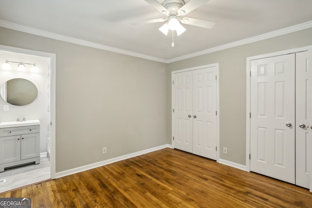 unfurnished bedroom featuring ceiling fan, crown molding, hardwood / wood-style floors, ensuite bathroom, and two closets