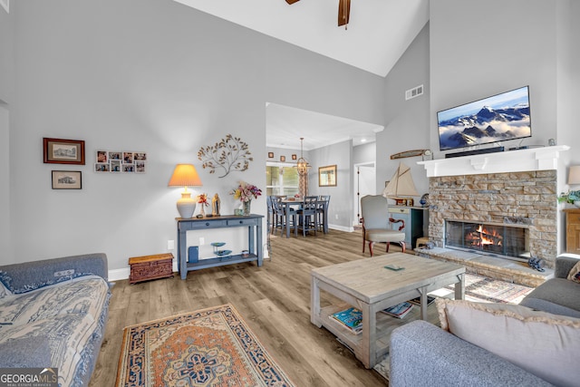 living room with ceiling fan, light hardwood / wood-style floors, a fireplace, and high vaulted ceiling