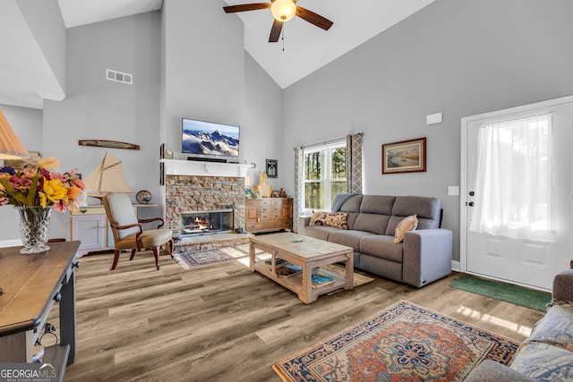 living room with a stone fireplace, ceiling fan, high vaulted ceiling, and wood-type flooring