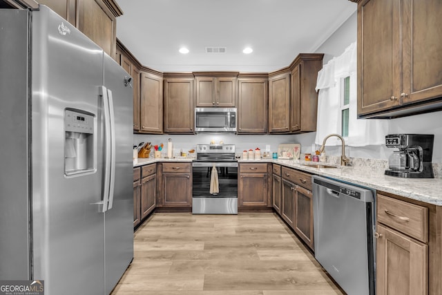 kitchen featuring sink, light stone counters, light wood-type flooring, and stainless steel appliances