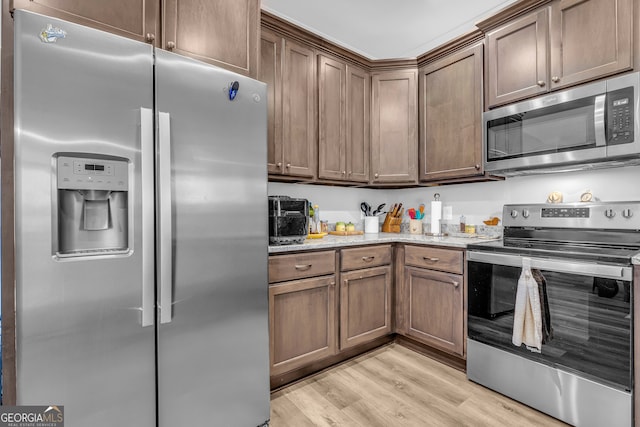 kitchen with stainless steel appliances, light hardwood / wood-style flooring, and light stone counters