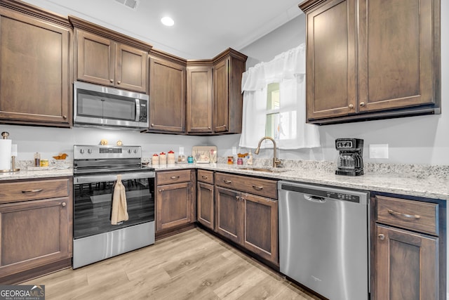 kitchen with crown molding, sink, light stone countertops, appliances with stainless steel finishes, and light hardwood / wood-style floors