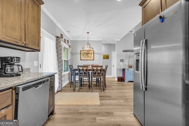 kitchen featuring crown molding, light wood-type flooring, decorative light fixtures, light stone counters, and stainless steel appliances