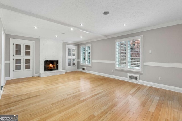 unfurnished living room featuring a textured ceiling, light hardwood / wood-style floors, ornamental molding, and a large fireplace