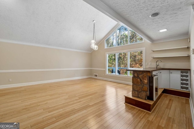 unfurnished living room with beverage cooler, crown molding, vaulted ceiling, a textured ceiling, and light wood-type flooring