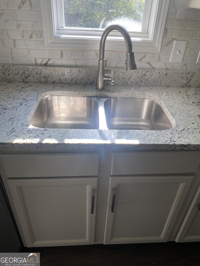 interior details with decorative backsplash, white cabinetry, light stone countertops, and sink