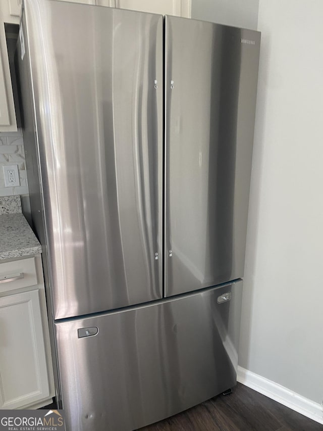 room details with backsplash, light stone counters, dark hardwood / wood-style floors, white cabinetry, and stainless steel refrigerator