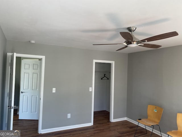 unfurnished bedroom featuring ceiling fan, a spacious closet, dark wood-type flooring, and a closet