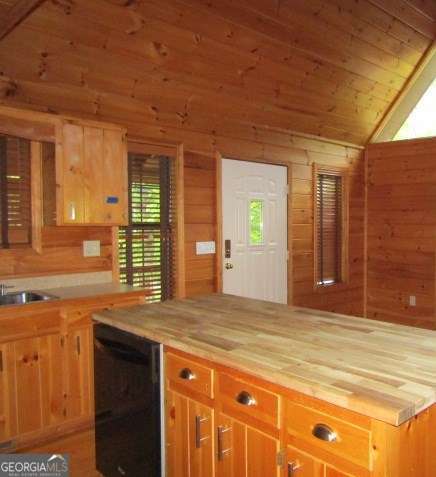 kitchen with dishwasher, sink, butcher block counters, and wood walls