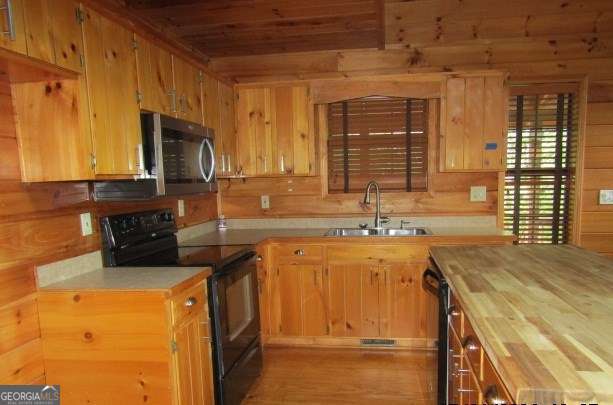 kitchen featuring sink, wooden walls, and black appliances