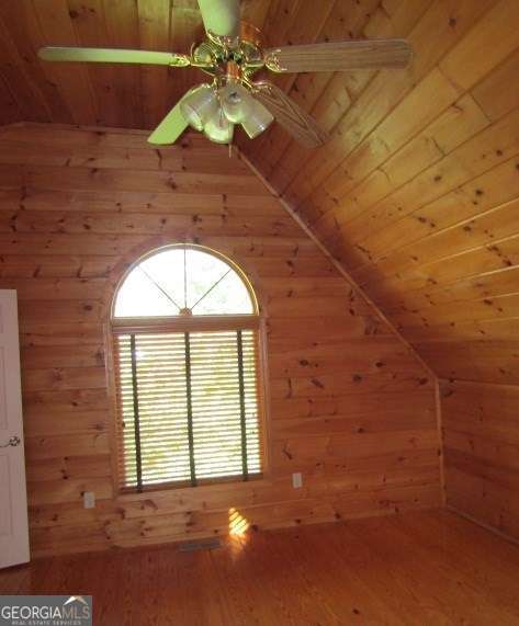 additional living space with wooden ceiling, wooden walls, vaulted ceiling, ceiling fan, and wood-type flooring