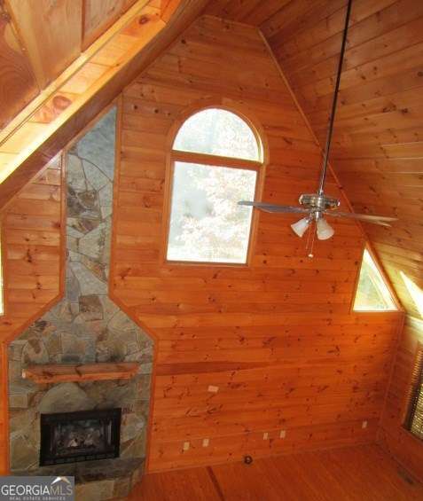 interior space with lofted ceiling, a stone fireplace, wooden walls, hardwood / wood-style flooring, and wood ceiling