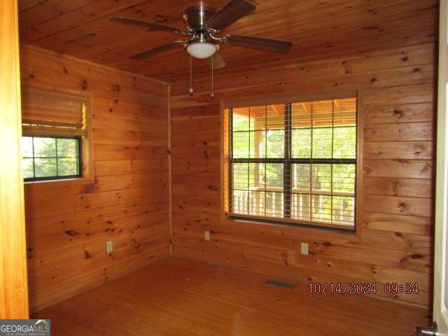 empty room with hardwood / wood-style floors, ceiling fan, wood walls, and wooden ceiling