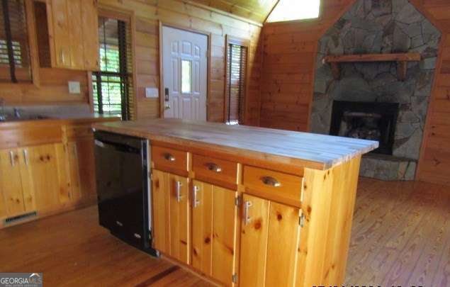 kitchen featuring black dishwasher, butcher block countertops, light hardwood / wood-style floors, wooden walls, and a fireplace