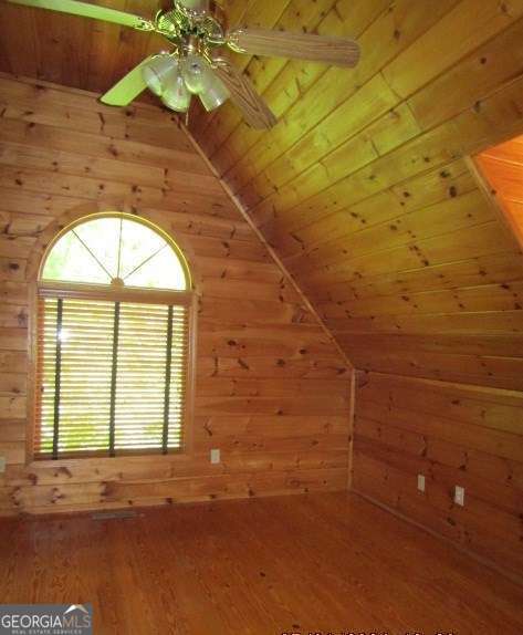 additional living space with wooden walls, vaulted ceiling, and hardwood / wood-style flooring