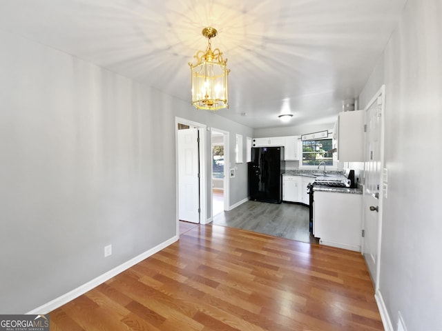 kitchen with black refrigerator, wood-type flooring, white cabinetry, and an inviting chandelier