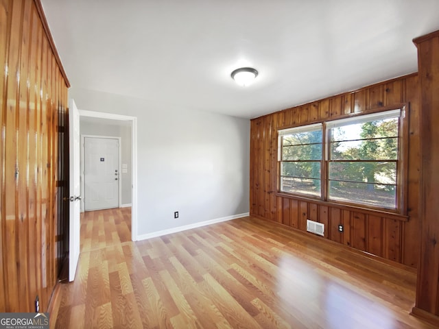 empty room with light hardwood / wood-style floors and wood walls