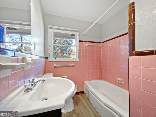 bathroom featuring vanity, wood-type flooring, tile walls, and tiled shower / bath