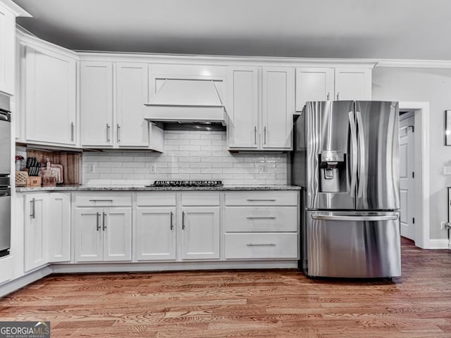 kitchen featuring stainless steel refrigerator with ice dispenser, black gas cooktop, custom range hood, and white cabinets