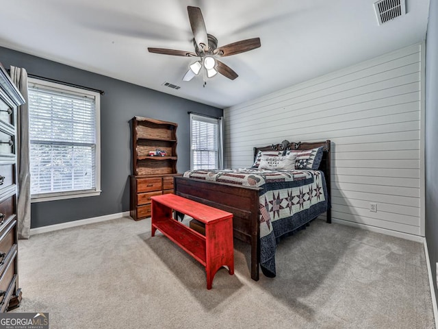 carpeted bedroom with ceiling fan and wood walls