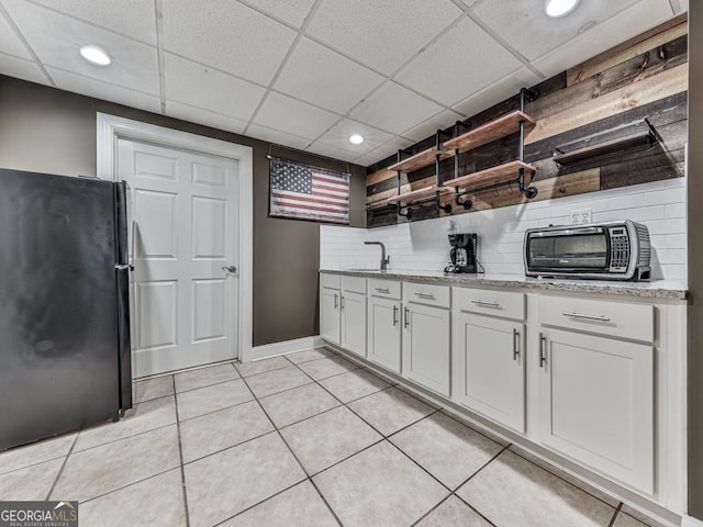 kitchen featuring black refrigerator, light tile patterned floors, white cabinetry, and decorative backsplash