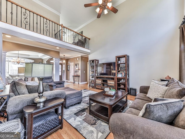 living room with ceiling fan with notable chandelier, decorative columns, a high ceiling, crown molding, and light wood-type flooring