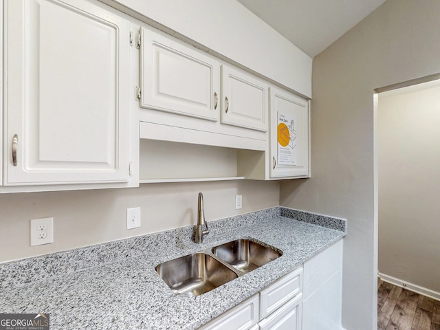 kitchen with wood-type flooring, light stone counters, white cabinetry, and sink