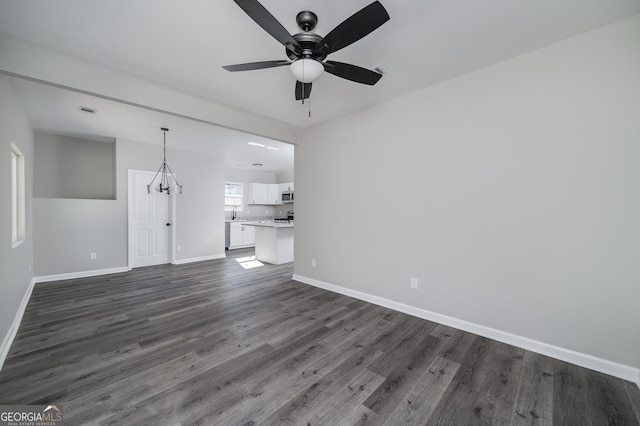 unfurnished living room featuring ceiling fan with notable chandelier and dark hardwood / wood-style flooring