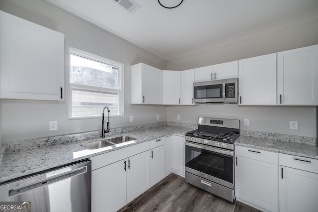 kitchen with white cabinets, sink, light stone countertops, appliances with stainless steel finishes, and dark hardwood / wood-style flooring