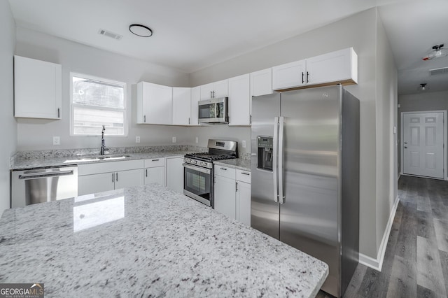 kitchen with white cabinets, sink, appliances with stainless steel finishes, light stone counters, and wood-type flooring