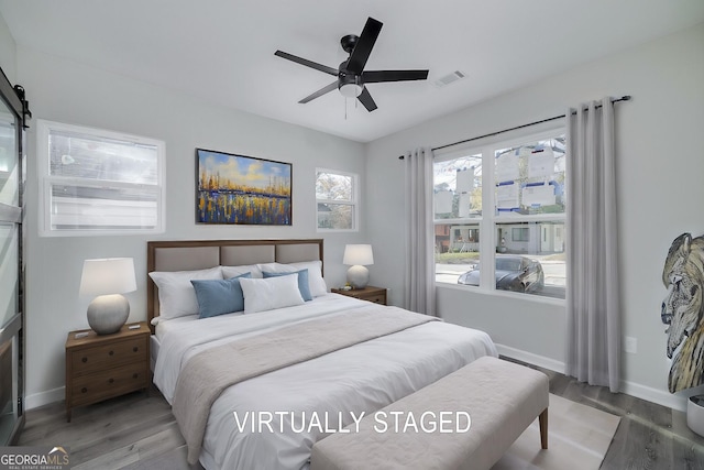 bedroom featuring hardwood / wood-style flooring, ceiling fan, and a barn door