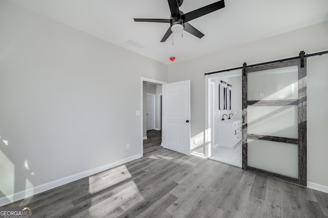 unfurnished bedroom featuring hardwood / wood-style floors, ceiling fan, a barn door, and sink