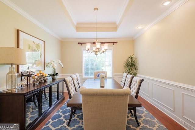 dining space featuring a tray ceiling, dark wood-type flooring, a notable chandelier, and ornamental molding