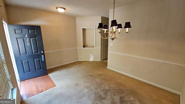 carpeted entrance foyer featuring a textured ceiling and an inviting chandelier