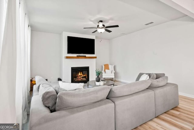 living room with visible vents, light wood-style flooring, baseboards, a ceiling fan, and a glass covered fireplace
