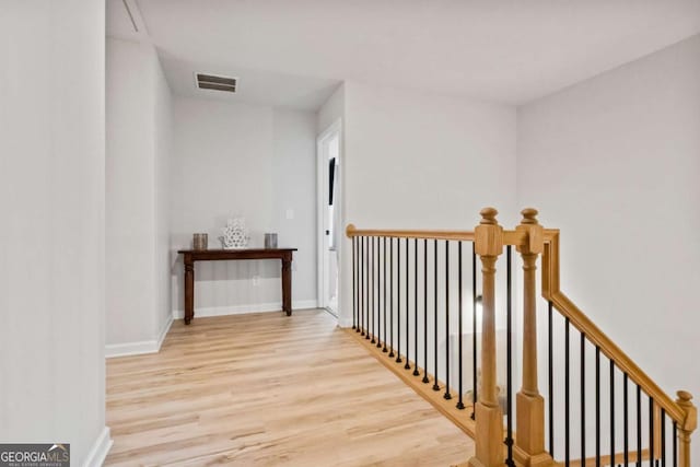 hall featuring wood finished floors, an upstairs landing, baseboards, and visible vents