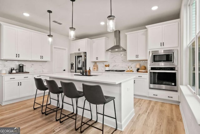 kitchen featuring wall chimney exhaust hood, a breakfast bar, appliances with stainless steel finishes, and white cabinets
