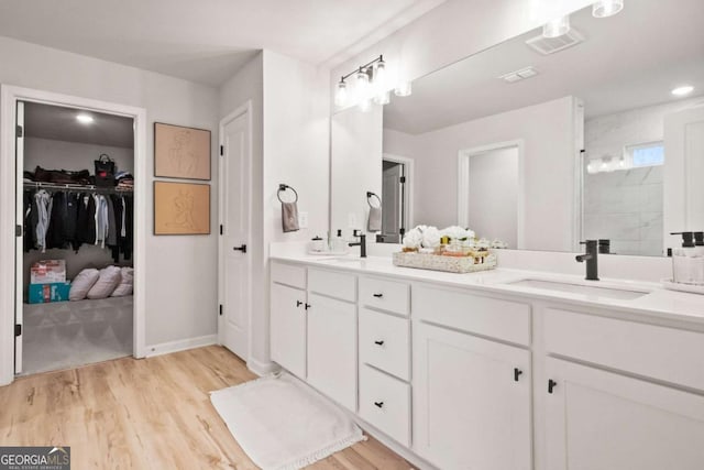 full bathroom featuring a tile shower, a spacious closet, a sink, double vanity, and wood finished floors
