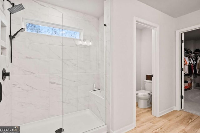 bathroom with a spacious closet, toilet, baseboards, a stall shower, and wood finished floors