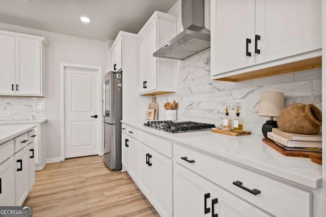 kitchen with white cabinets, light countertops, light wood finished floors, stainless steel appliances, and wall chimney exhaust hood