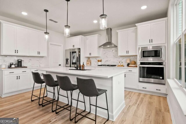 kitchen featuring white cabinets, wall chimney exhaust hood, decorative light fixtures, and appliances with stainless steel finishes