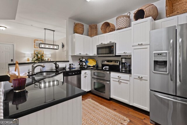 kitchen featuring white cabinets, decorative light fixtures, wood-type flooring, and appliances with stainless steel finishes