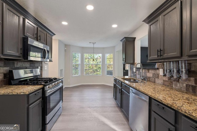 kitchen featuring sink, decorative backsplash, light stone countertops, dark brown cabinetry, and stainless steel appliances