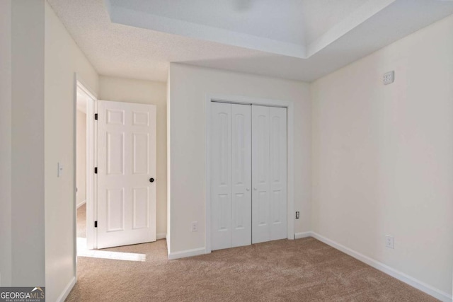 unfurnished bedroom featuring a textured ceiling, light colored carpet, and a closet