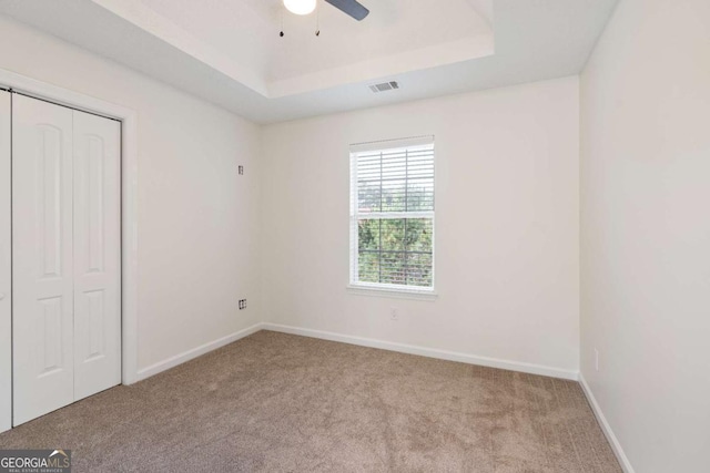 unfurnished bedroom featuring a closet, light colored carpet, a raised ceiling, and ceiling fan