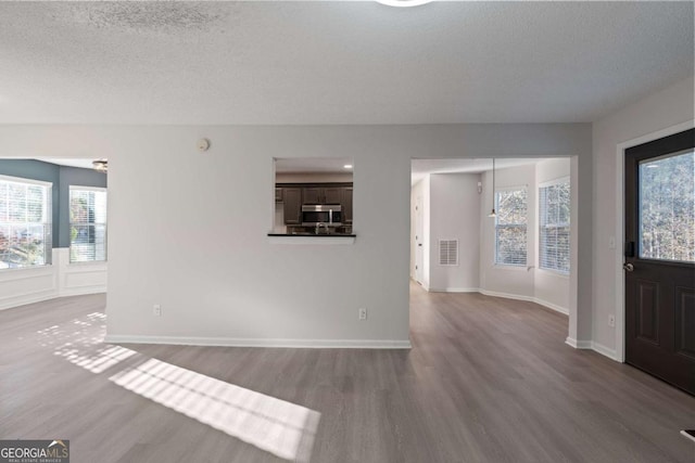 unfurnished living room with hardwood / wood-style flooring, plenty of natural light, and a textured ceiling