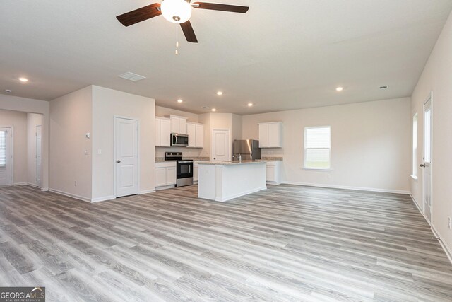 kitchen with ceiling fan, an island with sink, appliances with stainless steel finishes, light hardwood / wood-style floors, and white cabinetry