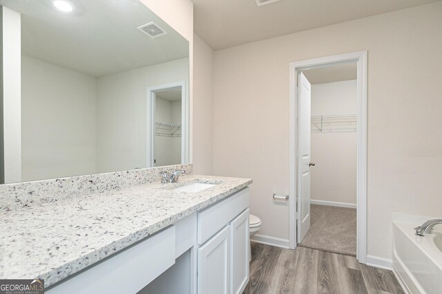 bathroom featuring a tub, vanity, wood-type flooring, and toilet