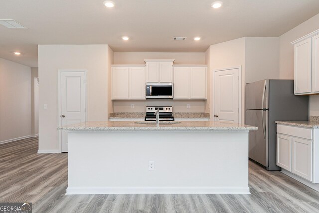 kitchen featuring light stone countertops, light hardwood / wood-style flooring, a kitchen island with sink, white cabinets, and appliances with stainless steel finishes