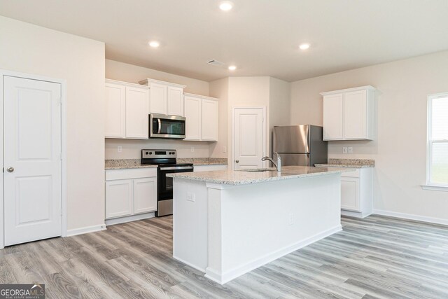 kitchen with light wood-type flooring, stainless steel appliances, sink, white cabinetry, and an island with sink